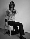 Die Atempädagogin Claudia Kaltenbach sitzt auf einem Hocker und zeigt eine Körperübung. Es ist eine Rumpfdrehung.